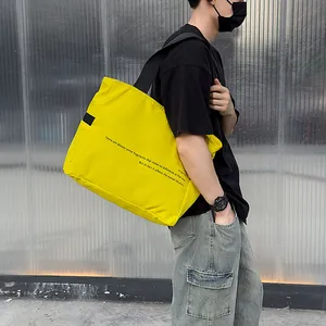 Detalle de un bolso tote grande de nailon amarillo con texto en modelo masculino
