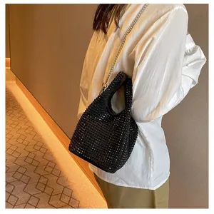 Close-up of a stylish black rhinestone bucket bag with a silver chain strap on a model