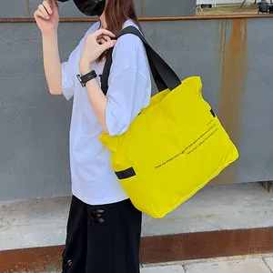 Vista detallada de un bolso tote grande de nailon amarillo con correas negras y texto
