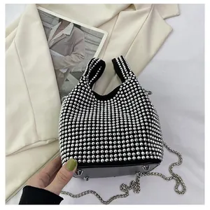 Detail of a black rhinestone bucket bag with silver chain strap on a white blazer