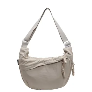 Detail of minimalist beige dumpling crossbody bag with adjustable white shoulder strap