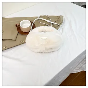 Primer plano de un bolso bandolera de felpa blanca tipo dumpling en una mesa blanca