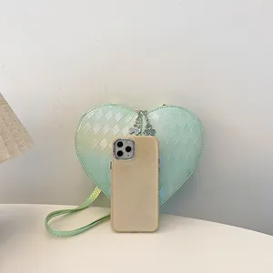 Größenvergleich der mintgrünen herzförmigen Tasche mit Rautenmuster und einem Smartphone