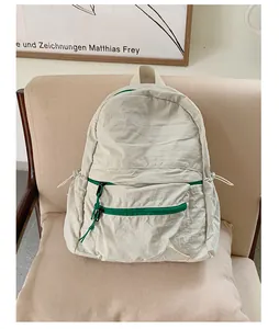 Close-up of a cream wrinkled nylon backpack with green zipper details on a chair
