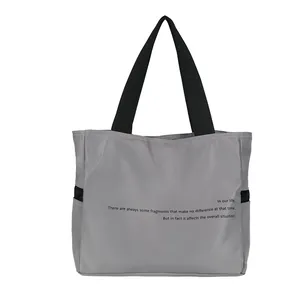 Vista detallada de un bolso tote de nailon gris con impresión de texto en inglés
