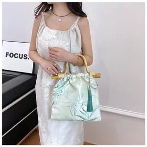 Elegante borsa a mano in stile cinese con manici in bambù e nappa verde sul modello.