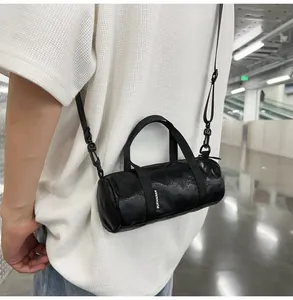 Close-up of a mini black cylinder crossbody bag worn on a white textured t-shirt