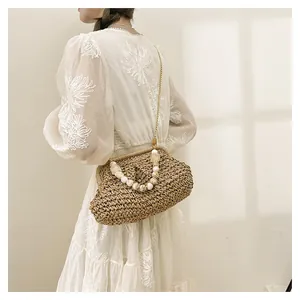 Dettaglio di una borsa in paglia con manico di perle e catena d'oro su una modella.