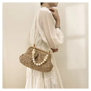 Elegante borsa di paglia con manico di perle e catena su un abito estivo bianco.