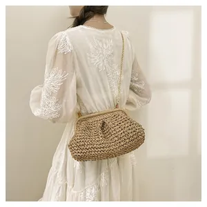 Borsa a mano in paglia intrecciata con catena dorata su un elegante abito bianco
