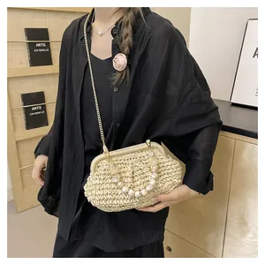 Primo piano di una borsa in paglia intrecciata con manico di perle e tracolla a catena
