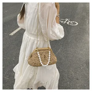 Dettaglio della borsa clutch in paglia con manico di perle sopra un abito bianco.