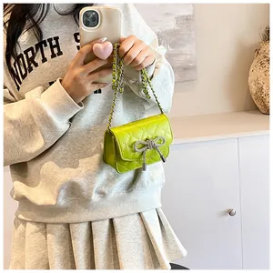 Detailopname van limoengroene gewatteerde crossbodytas met kristallen strik en ketting.