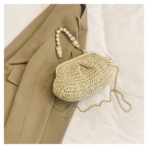 Primo piano di pochette in paglia con manico di perle e catena d'oro su cappotto beige