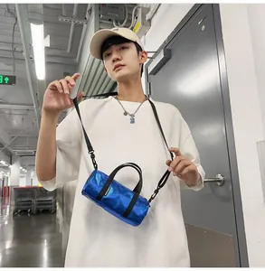 Model carrying a shiny blue mini cylindrical crossbody bag in an urban corridor