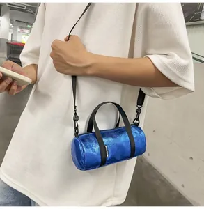 Detail view of a mini metallic blue cylindrical crossbody bag worn over a white shirt.