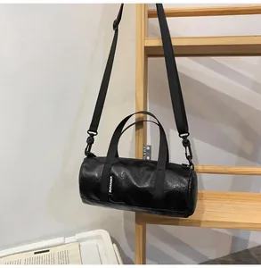 Macro detail of black mini cylinder crossbody bag with glossy finish and logo tag.