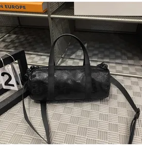 Macro view of a glossy black mini cylindrical crossbody bag showing material texture.
