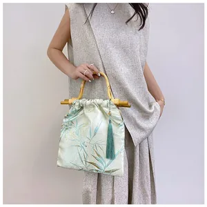 Dettaglio borsa in stile orientale con manico in bambù e stampe floreali in seta verde acqua.