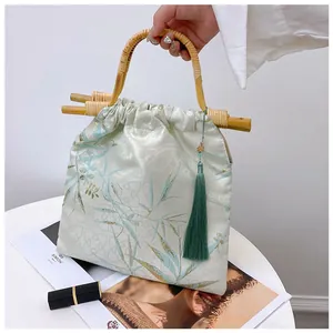 Dettaglio borsa vintage in stile orientale con manico in bambù e nappa verde scuro.