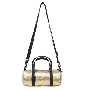 Casual mini metallic gold cylinder crossbody bag with black handles and long strap