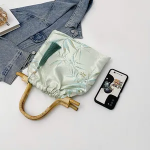 Dettaglio di una borsa stile cinese con manici in bambù e decorazione a nappa verde.