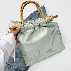 Dettaglio di una borsa a mano plissettata in stile orientale con manici in bambù e stampe.