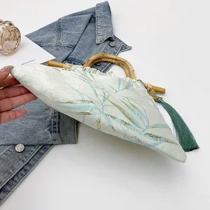 Dettaglio borsa stile cinese con manico in bambù e nappa di seta verde decorativa.