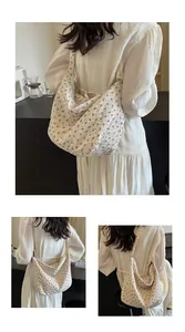 Detalle de un bolso tote con flores en crema llevado por una modelo con vestido blanco