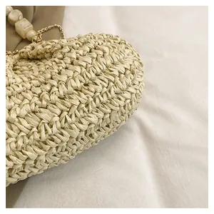 Primo piano di borsa in paglia beige intrecciata con catena di perle dorate