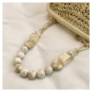 Dettaglio borsa di paglia con tracolla in perle effetto marmo e catena dorata.