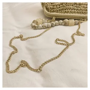 Dettaglio di una tracolla a catena dorata con perle marmorizzate su una borsa di paglia