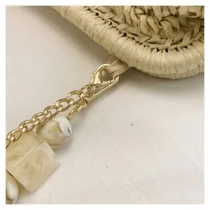 Macro detail of marble-textured beads and gold chain on a straw woven beach bag