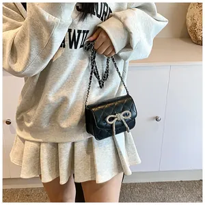 Detail van zwarte gewatteerde crossbodytas met strass strik en metalen kettingriem