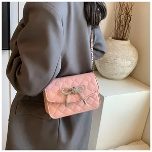 Detail van een roze gewatteerde crossbodytas met een strass-strik en metalen ketting