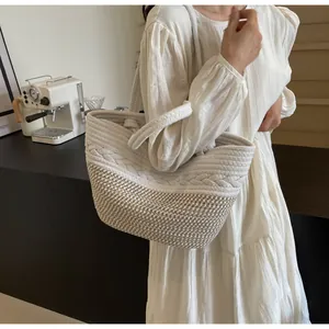Détail d'un sac cabas bicolore en paille avec une robe d'été blanche légère.