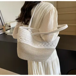 Détail d'un sac cabas en paille tissée bicolore porté à l'épaule pour les vacances