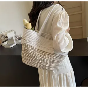 Sac fourre-tout en paille tressée beige et blanc porté en bandoulière au café.