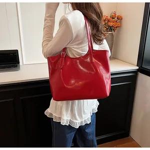 Large red glossy leather underarm tote bag worn by a model in a stylish setting
