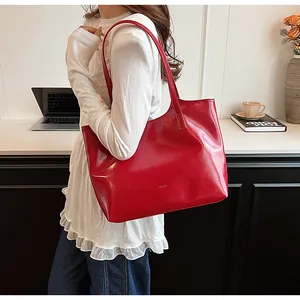 Detail of a large red glossy tote bag worn as a shoulder bag in a modern interior.