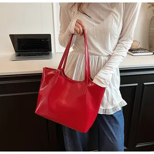 Detailed view of the red glossy leather tote bag held by a model in a casual setting