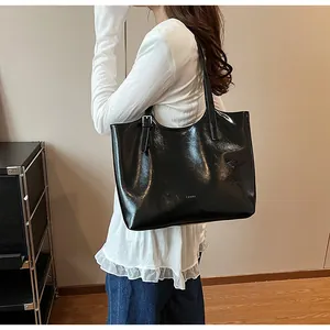Minimalist large black glossy leather underarm tote bag worn on shoulder by model.