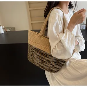 Détail d'un sac cabas en paille tressée avec un motif bicolore et des poignées.