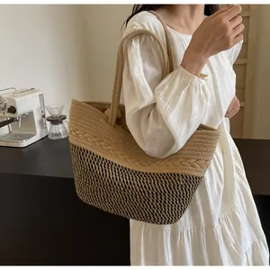 Gros plan d'un sac cabas en paille tissé bicolore porté par un modèle en robe blanche.