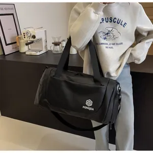 Large black travel duffel bag with shoulder strap held in a modern lifestyle setting