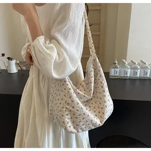 Detalle de un bolso hobo crema con estampado floral llevado al hombro por una modelo