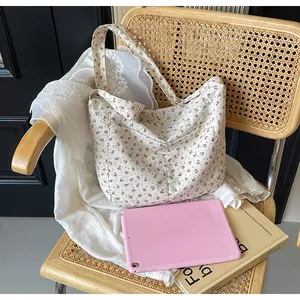 Bolso de tela con estampado floral en silla de madera junto a tableta rosa y libro