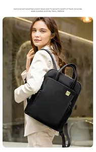 Elegant model wearing a minimalist black square backpack with gold-toned metal logo plate.