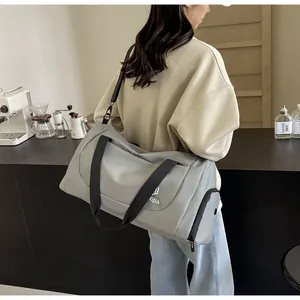 Lifestyle detail showing a large gray travel duffel bag worn by a woman in a cafe