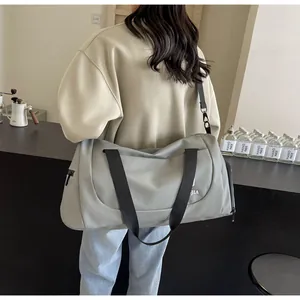 Detailed view of a large grey travel duffle bag worn as a shoulder bag in a cafe.